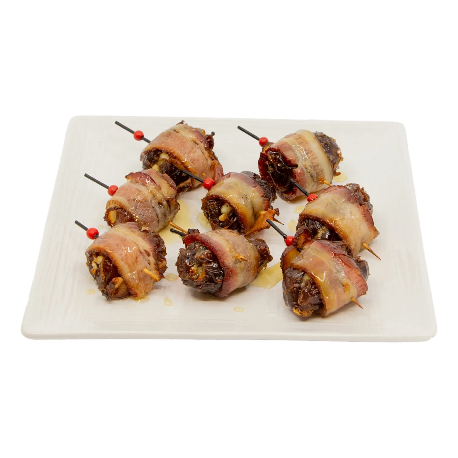 Golden bacon-wrapped, gorgonzola stuffed dates, secured with red-tipped toothpicks, arranged on a white rectangular plate; a savory appetizer presented against a clean white background.