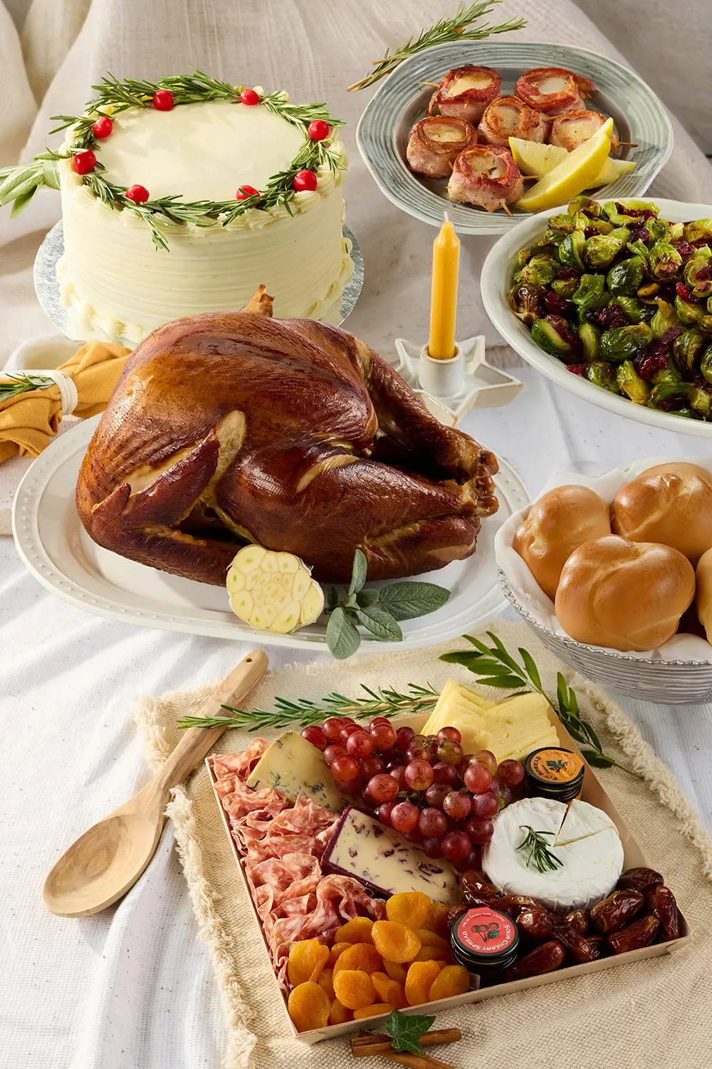 A festive holiday feast features a golden roast turkey, decorated cream cake, roasted vegetables, rolls, and a cheese-and-fruit board, arranged warmly on a linen-covered table.