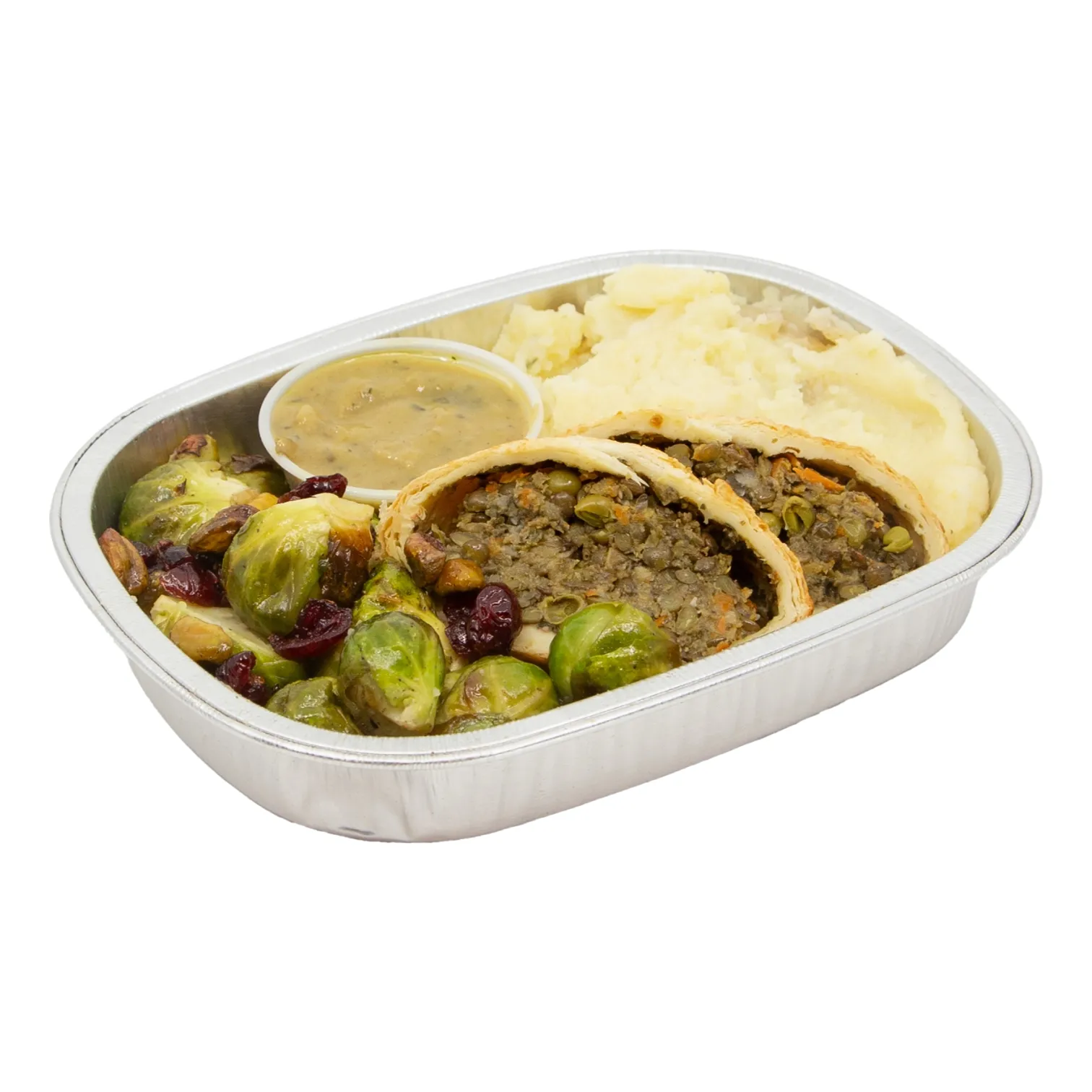 A foil tray holds lentil wellington, mashed potatoes, brussels sprouts, and savory mushroom gravy; a hearty, comforting prepared dinner.