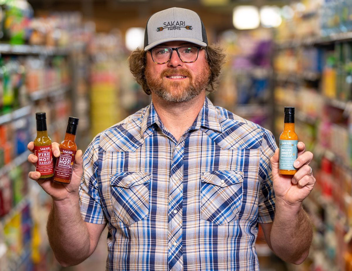 Sakari Farms representative holding up three bottles of hot sauce