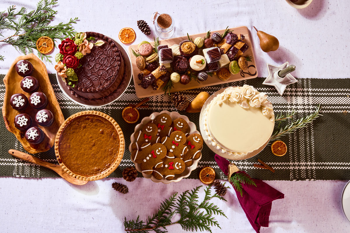 Festive holiday spread from Market of Choice featuring oysters, roasted veggies, mashed potatoes, croquettes, stuffing, and charcuterie, surrounded by candles, pomegranates, and holiday décor.