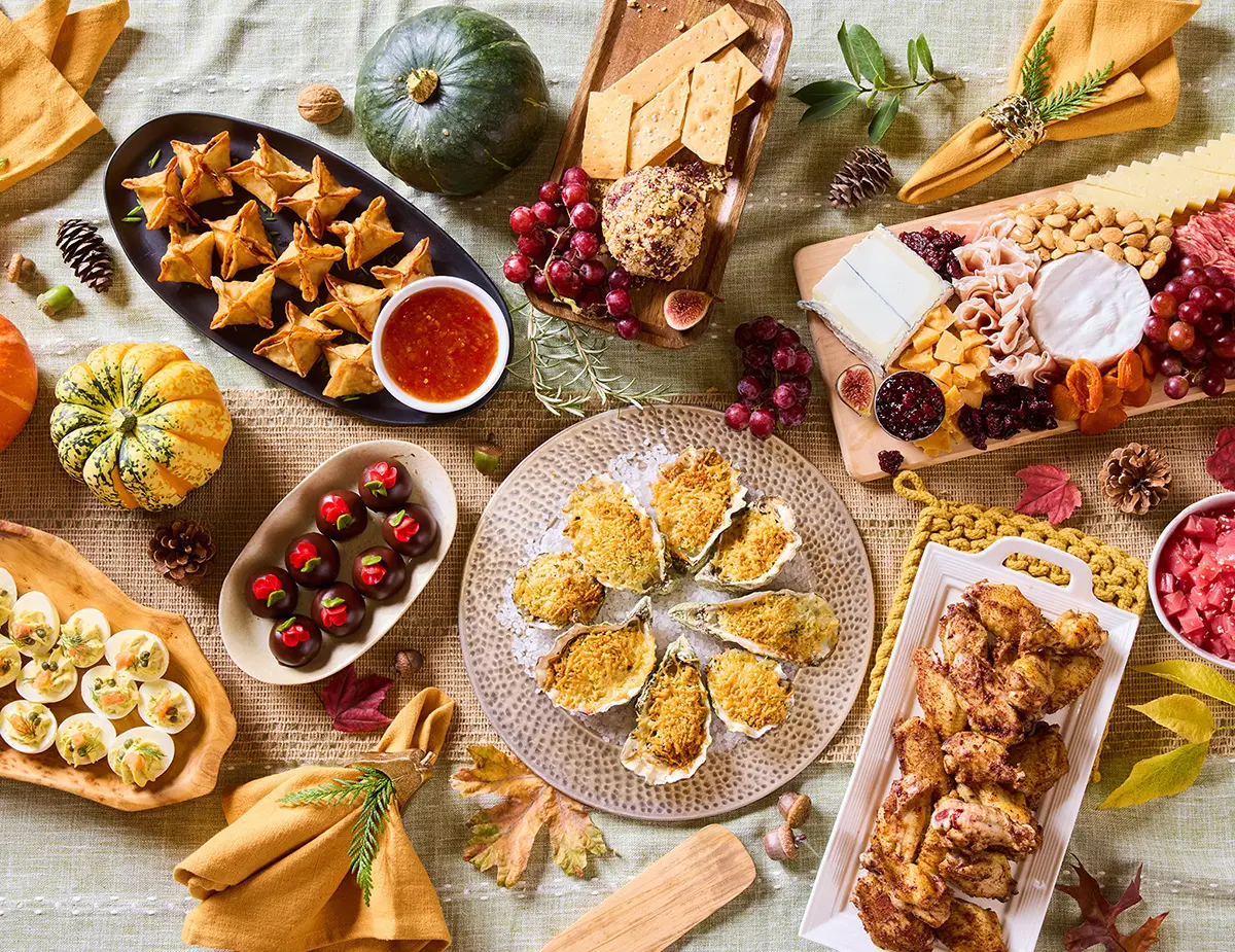 Fall appetizer spread featuring oysters, deviled eggs, stuffed mushrooms, charcuterie and cheese, chicken skewers, fruit and seasonal pumpkins on a rustic table.